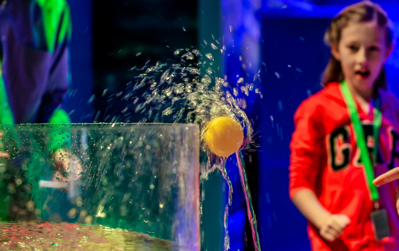 Bildet viser en jente som kaster en gul ball i en beholder med vann